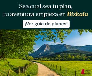 Un camino de tierra atraviesa un campo verde con árboles y se dirige hacia una montaña bajo un cielo azul. El texto dice: Sea cual sea tu plan, tu aventura empieza en Bizkaia. ¡Ver guía de planes!.