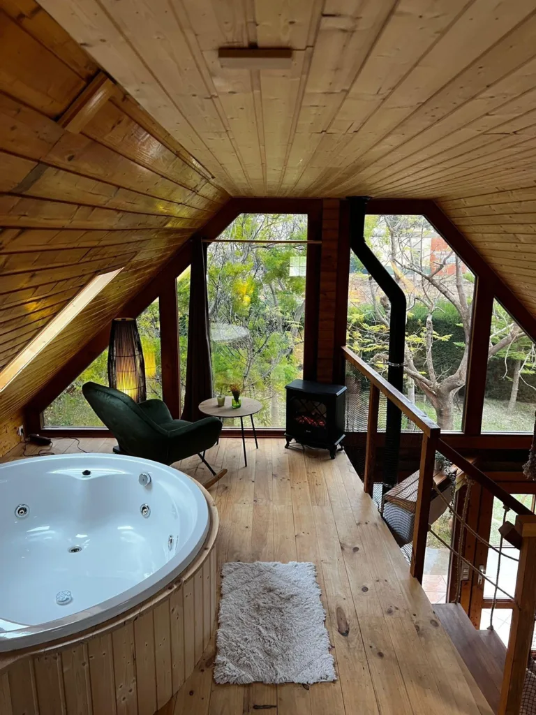 Cabaña de madera con jacuzzi, ventanal y sillones con vistas al jardín