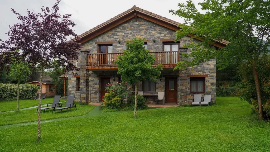 Casa rural de piedra con un jardín verde y diferentes árboles