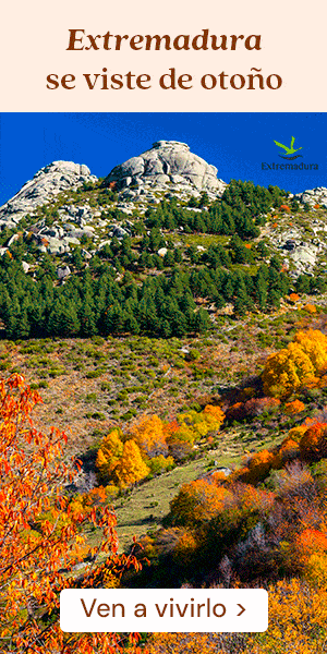 Una montaña rocosa con pinos verdes y un follaje otoñal de colores vivos. Texto en español: «Extremadura se viste de otoño. Ven a vivirlo». Logotipo de Turismo de Extremadura en el cielo.