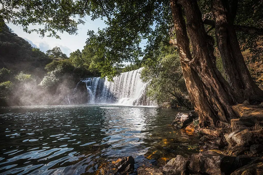 La ruta que comienza en una piscina natural, remonta un río entre chopos y termina en una cascada de 16 metros