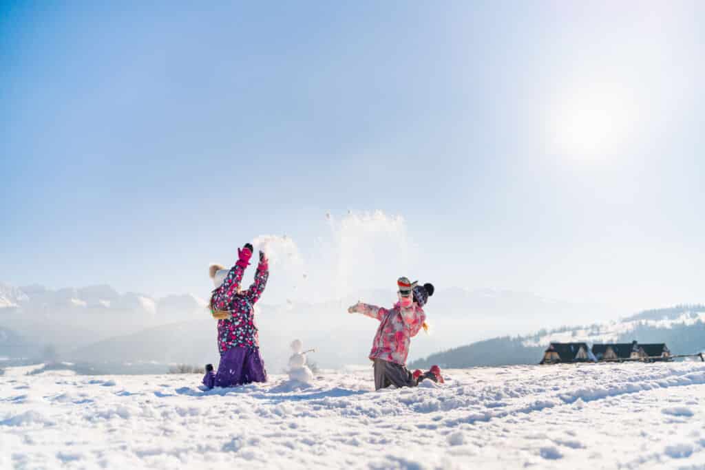 Niños lanzando nieve al aire en un paisaje nevado.