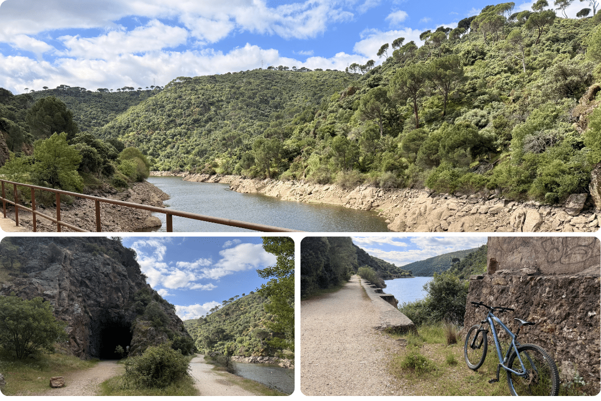 Un río serpentea por un paisaje verde y montañoso de Asturias bajo un cielo azul. Abajo, una bicicleta se apoya en un muro junto a un camino de tierra, y otro camino conduce a un túnel en la base de una ladera rocosa.