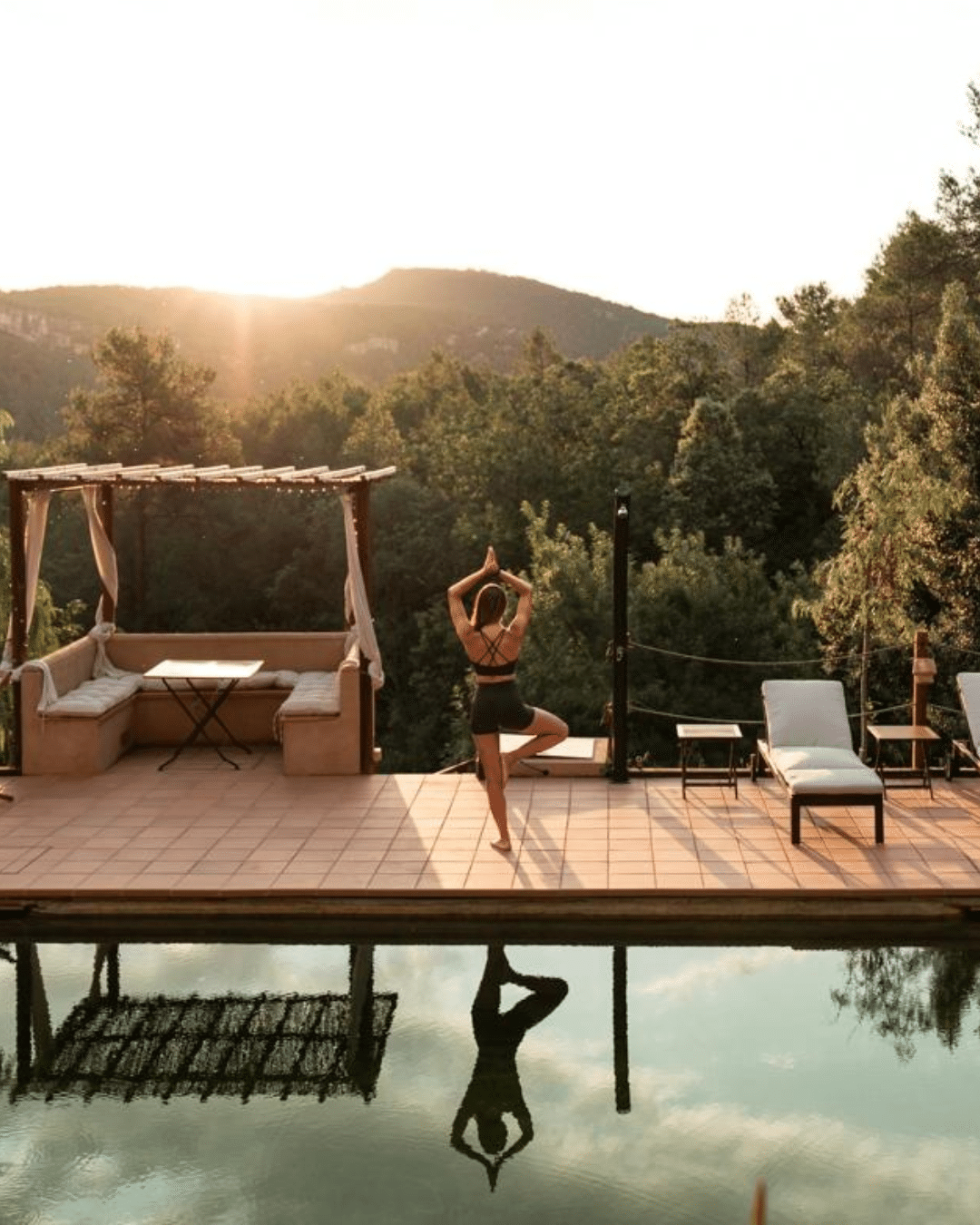 Una persona realiza la postura del árbol en una terraza con vistas a una piscina y al bosque al atardecer, mientras disfruta de un verano rural en la Comunitat Valenciana.