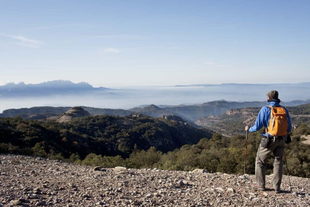 Un excursionista, con una mochila y bastones de senderismo, contempla una extensa y brumosa cordillera.