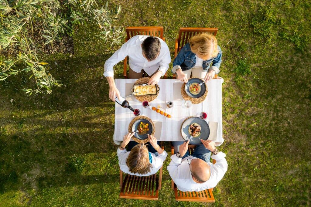 Vista aérea de cuatro personas cenando en una mesa cuadrada al aire libre, situada sobre el césped.