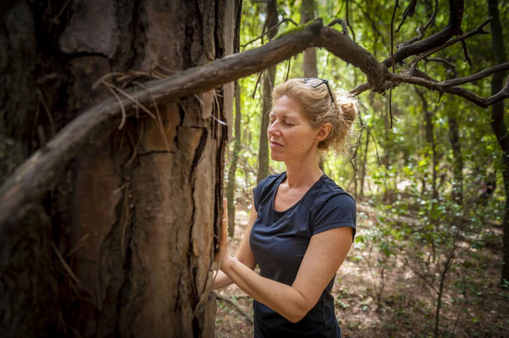 Una mujer, con los ojos cerrados, acaricia el tronco de un árbol enorme en un bosque.