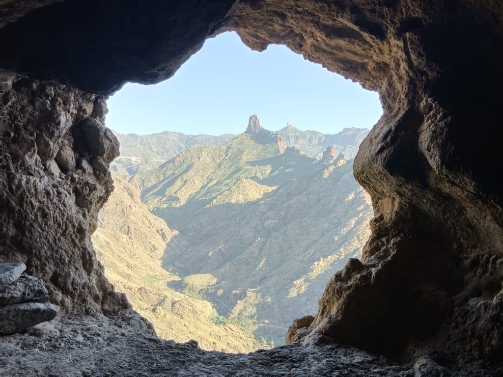 Esta cueva de Acusa se abre a la cuenca volcánica de Bentayga, presidida por el roque Bentayga. Al fondo, el roque Nublo.